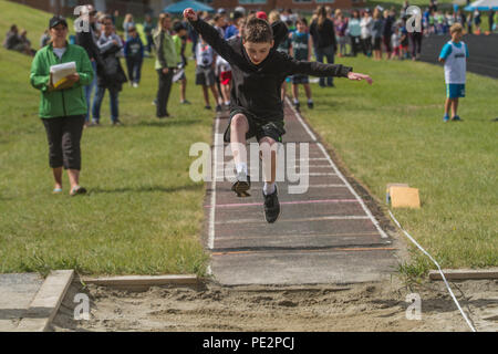 Jeune garçon en compétition dans track & field's trple saut, portant des shorts et capuche. Pris dans l'air. Parution du modèle Banque D'Images