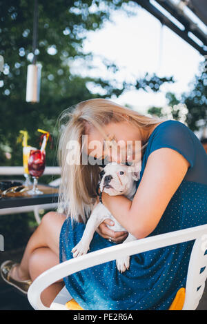 Jeune fille blonde dans la cafétéria tenue adorable chiot bouledogue français. Banque D'Images