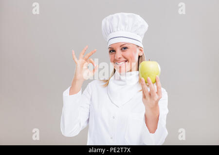 Belle femme chef est montrant ok sign et apple sur fond gris. Banque D'Images