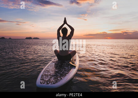 Yoga sur le SUP, silhouette de l'homme assis dans la position du lotus sur stand up paddle board Banque D'Images