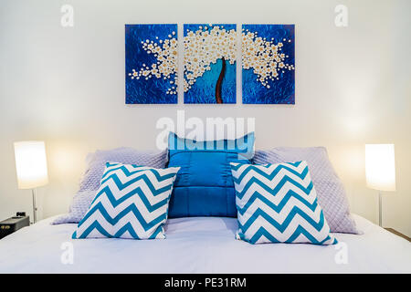 Grand lit avec literie et oreillers bleu vif dans une chambre moderne, art peinture murale et lumières Banque D'Images