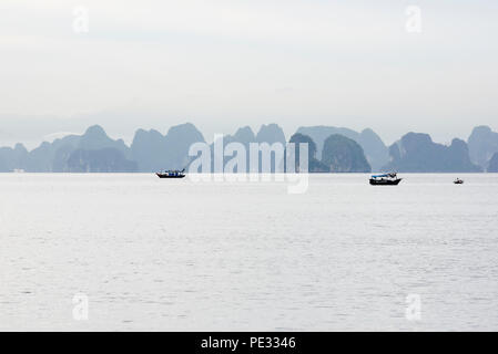 Emplacement calme et pittoresque du paysage marin de la Baie d'Halong, Vietnam du Nord, avec des petits bateaux de pêche silhouetté contre Misty Blue Mountains en arrière-plan. Couleurs sourdes Banque D'Images