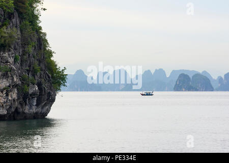 Un petit bateau de pêche en près de silhouette au repos entre gamme d'îlots dans la baie d'Halong, Vietnam du Nord, contre les montagnes de la bleuté misty backgroun Banque D'Images