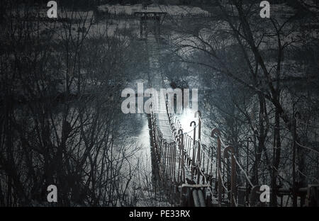 Sombre Creepy vieux pont suspendu sur la rivière dans le brouillard. Arrière-plan de l'halloween. Banque D'Images