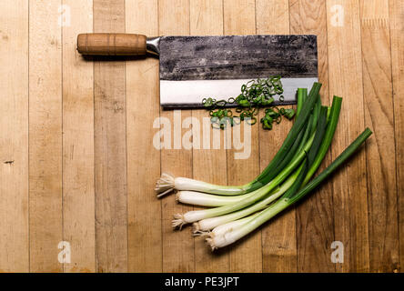 Couteau chinois avec les oignons verts sur une planche à découper en bois. Banque D'Images