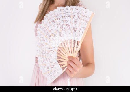 Belle jeune femme en robe de dentelle blanc crème holding ventilateur isolé sur fond blanc. La chaleur de l'été et concept. Close up, selective focus Banque D'Images