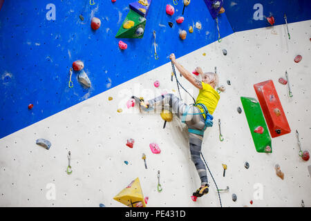 Photo de l'arrière de la sportive des jeunes en T-shirt jaune brouille sur mur d'escalade à workout Banque D'Images