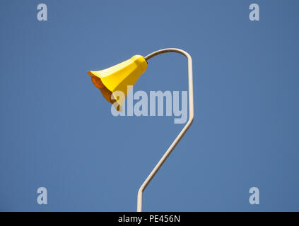 Image en couleur d'une ancienne lampe en forme de fleur jaune sur une courbe et coudée metal lampadaire, tourné à partir de ci-dessous contre un ciel bleu clair Banque D'Images