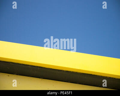 Couleur se rapprochant du bord de la toiture jaune d'une cabane de plage, tourné à partir de ci-dessous contre un ciel bleu clair Banque D'Images