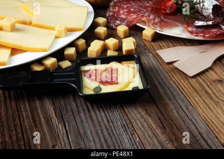 Délicieux fromage à raclette fondue suisse traditionnel sur les dés de pomme de terre au four ou bouillie servi dans des poêlons avec du salami. Banque D'Images