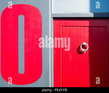 De couleur rouge avec une porte en bois rond en métal un heurtoir, à côté d'un mur peint en gris avec un grand peint rouge zéro sur elle Banque D'Images
