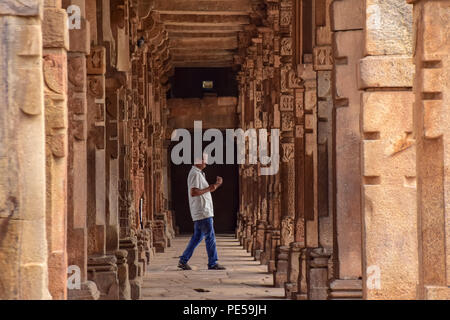 Un homme marche entre la série de colonnes à l'intérieur -Sculputed Quwwat ul -l'Islam mosquée de Qutub Complex à Delhi en Inde. Qûtb Minâr Comité permanent 73 mètres de haut à Delhi, est le plus haut minaret de briques et site du patrimoine de l'UNESCO. Il représente l'Indo -style architectural islamique, construit par Qutb-ud-Din Aibak comme une victoire Tower en 1192 A.D. Banque D'Images