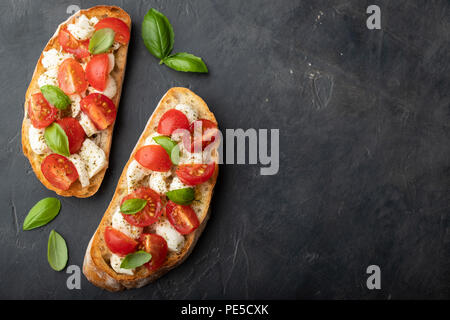 Bruschetta à la tomate, mozzarella et basilic sur un fond noir. Apéritif italien traditionnel ou un en-cas, l'antipasto. Vue de dessus avec l'exemplaire de l'espace. Mise à plat Banque D'Images