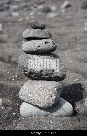 Des pierres empilées équilibré ou des cailloux sur une plage de sable noir. Banque D'Images