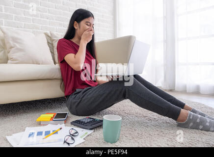 Offres et demandes de missions femme asiatique bâillement tout en travaillant sur un ordinateur portable avec un étage de séance paperasserie et se penchant au canapé,travail à domicile accueil concept Banque D'Images