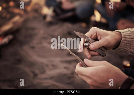 L'insouciance heureuse jeunes amis de s'amuser et de boire une bière par Bonefire sur la plage alors que le soleil commence à définir des filtres Banque D'Images