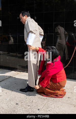Une femme bouddhiste bhoutanais aide un homme a mis sur sa longueur complète traditionnelle les vêtements. Dans la région de Woodside, Queens, New York. Banque D'Images