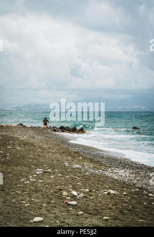 Scène de plage typique de l'île de Crète. De jeune femme marchant le long de la plage. Vue vers l'océan. Avec les montagnes en arrière-plan sur un ciel nuageux da Banque D'Images