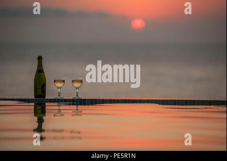 Champagne par une piscine à débordement au coucher du soleil Banque D'Images