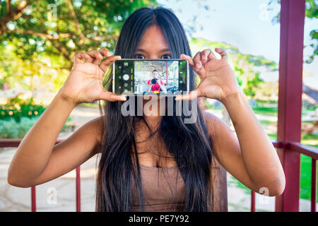 Jeune fille belle holding phone dans la main et jouer avec des applications dans l'app pour smartphone poster photo dans les médias sociaux Banque D'Images