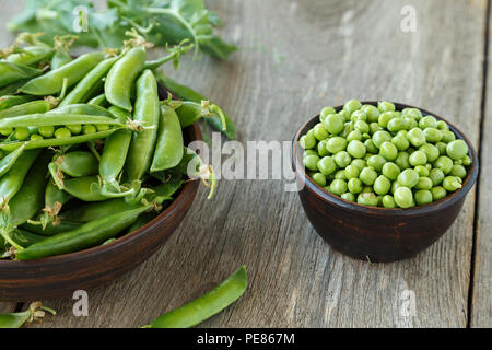 Les jeunes pois dans une plaque d'argile sur une table en bois. à côté d'une plaque sont un pea pods. Banque D'Images