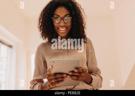 Portrait of a businesswoman in formal attire holding a tablet pc dans les mains. Curly haired woman entrepreneur de spectacles à la maison avec un tablet pc en h Banque D'Images