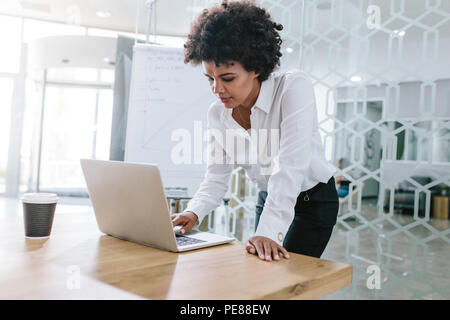 Jeune femme africaine article par table et en regardant son portable. Business Woman working on laptop computer dans la salle de réunion. Banque D'Images