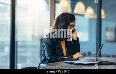 Business Woman sitting travaillant au bureau et talking on mobile phone. Femme d'affaires occupé à travailler à son bureau. Banque D'Images