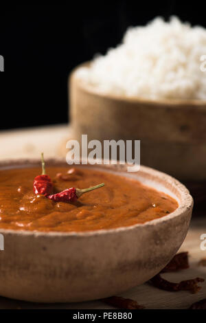 Libre d'un bol avec un poulet korma curry et un bol avec du riz cuit sur une table en bois rustique Banque D'Images