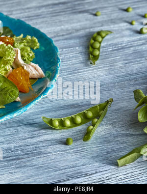 Pois verts fraîchement cueillis et la partie de la plaque en céramique bleue avec de la salade sur une table en bois gris avec de l'espace pour le texte. Banque D'Images