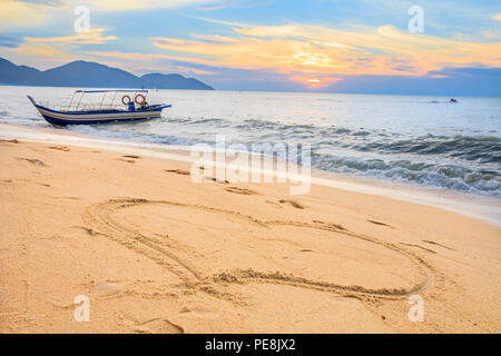 Tropical Beach en Malaisie avec un coucher de soleil dans l'arrière-plan, d'un bateau dans l'océan et un coeur dessiné dans le sable Banque D'Images