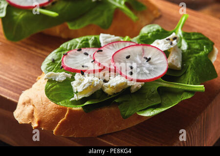 Sandwichs sains lumière avec du pain toasts, fromage doux et des radis, des épinards biologiques recueillies sur une planche de bois.