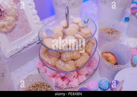 Glass cake stand avec de délicieux macarons français pastel, petites meringues rose et profiteroles Banque D'Images