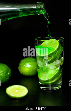 Verre de limonade verte froide avec de la glace et les limes vert frais mûrs sur fond noir. Limonade fait maison. Cocktail Mojito ou l'estragon. Le printemps et l'été Banque D'Images