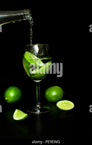 Les boissons rafraîchissantes d'été et concept. wineglass de boisson froide avec de la glace et tranche frais mûrs limes vert sur fond noir. Limonade fait maison. Moj Banque D'Images