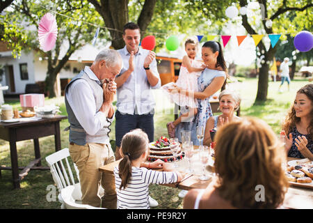 Un homme avec une famille élargie à la recherche sur le gâteau d'anniversaire, de pleurer. Banque D'Images