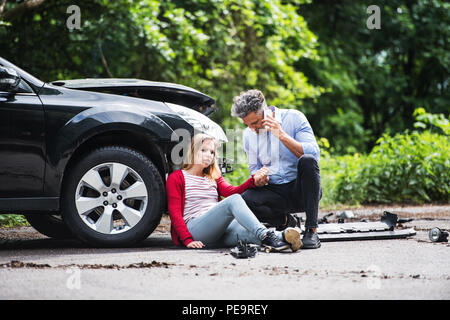 Jeune femme de la voiture après un accident et un homme de passer un appel téléphonique. Banque D'Images