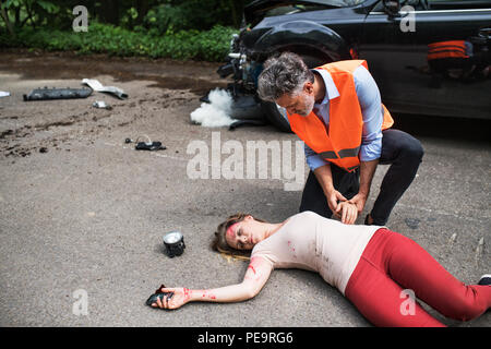 Un homme aide une jeune femme allongée, inconsciente sur la route après un accident de voiture. Banque D'Images