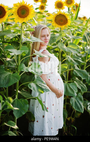 Blonde mère enceinte en champ de tournesols. Heureux moments de la grossesse. Banque D'Images