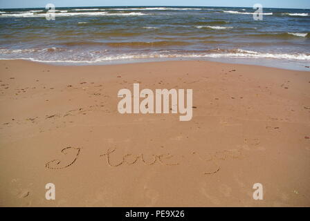 Mots 'Je vous aime' magnifiquement à la main sur du sable rouge sur une plage avec la mer, le ciel et les vagues dans la partie supérieure, l'Île du Prince Édouard Banque D'Images