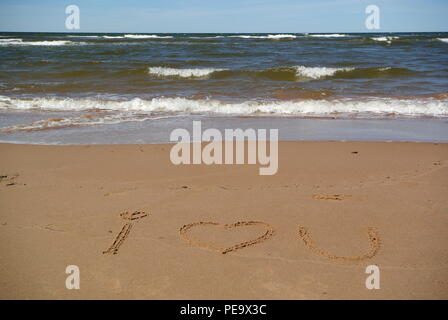 Mots 'Je t'aime' (symbole coeur magnifiquement) à la main sur du sable rouge sur une plage avec la mer, le ciel et les vagues dans la partie supérieure, l'Île du Prince Édouard Banque D'Images