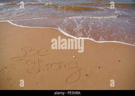 Un beau message de motivation "être fort" à la main sur le sable rouge sur une plage avec une vague, l'Île du Prince Édouard. Banque D'Images