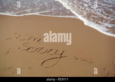 Un beau message appology 'Je suis désolé' dans un style manuscrite cursive sur le sable rouge sur une plage avec une vague venant dans la partie supérieure, PEI, Canada Banque D'Images