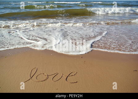 Le mot 'Amour' dans un style manuscrite cursive sur le sable rouge sur une plage avec la mer bleue et une vague dans la partie supérieure, l'Île du Prince Édouard Banque D'Images