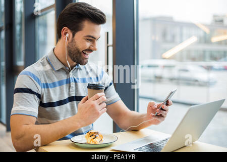 Matin merveilleux. Belle heureux homme joyeuse portant des écouteurs et l'écoute de sa chanson préférée pendant le petit-déjeuner dans le café Banque D'Images