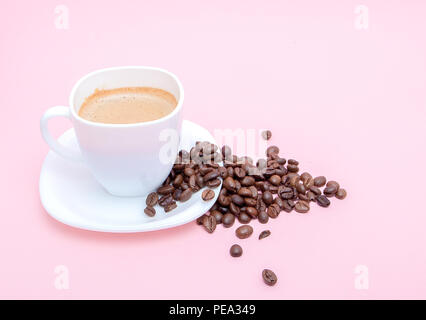 Grains de café torréfié dispersés dans une tasse sur un fond rose, copiez l'espace. Banque D'Images