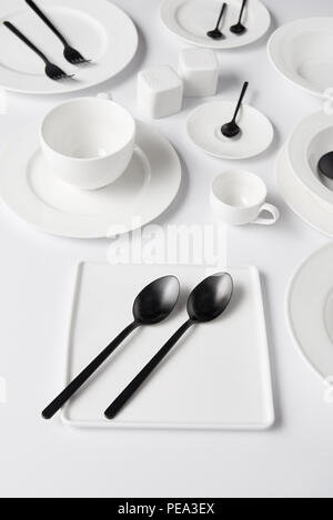 Focus sélectif des différentes assiettes, tasse, bol, pot de sel et poivre caster, fourche avec cuillères de table blanc sur Banque D'Images