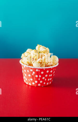 Une tasse de papier rouge avec pop-corn contre fond orange avec spot éclairage, faible profondeur de champ, l'accent sur le maïs soufflé. Banque D'Images