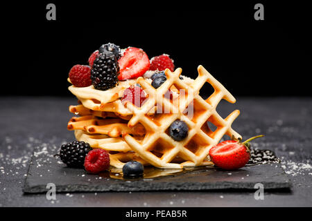 Photo de gaufrettes viennoises frais aux fruits rouges avec du sucre en poudre sur tableau noir sur fond blanc Banque D'Images