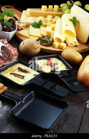 Délicieux fromage à raclette fondue suisse traditionnel sur les dés de pomme de terre au four ou bouillie servi dans des poêlons avec du salami. Banque D'Images
